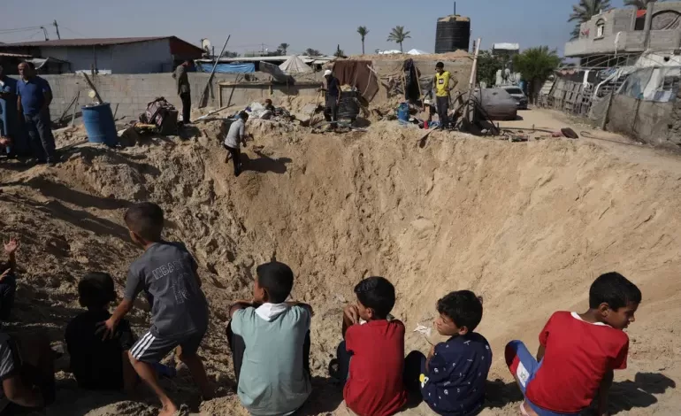 Palestinian children sit at the edge of a crater after an Israeli air strike in Khan Younis, southern Gaza Strip [File: Jehad Alshrafi/AP]