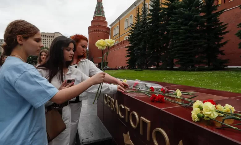 People lay flowers as tribute to the victims of Sunday's attack on a memorial bearing the word Sevastopol in Moscow