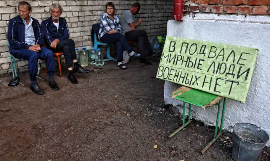 residents of Ukrainian -controlled Russian town of Sudzha sitting next to a sign reading;there are civilians in the basement