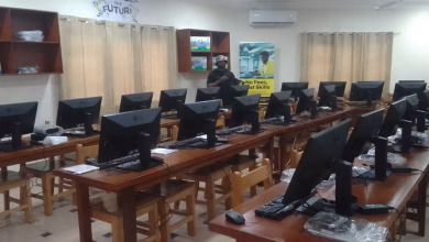 A computer laboratory with rows of desktop monitors on wooden desks and a person standing near the back of the room.