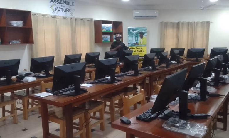 A computer laboratory with rows of desktop monitors on wooden desks and a person standing near the back of the room.