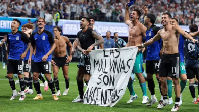 A group of football players celebrate on a pitch while holding a banner in front of a stadium crowd.