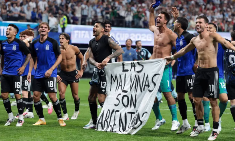 A group of football players celebrate on a pitch while holding a banner in front of a stadium crowd.