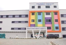 Exterior view of a multi-storey children's hospital building with a colourful central facade, vehicles at the entrance, and an outpatient department sign.