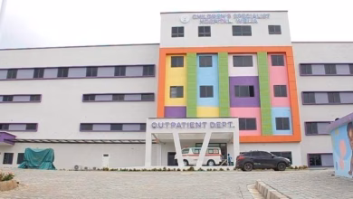 Exterior view of a multi-storey children's hospital building with a colourful central facade, vehicles at the entrance, and an outpatient department sign.