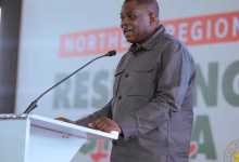 A man speaks at a lectern with a microphone in front of a presentation backdrop.