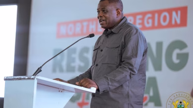 A man speaks at a lectern with a microphone in front of a presentation backdrop.