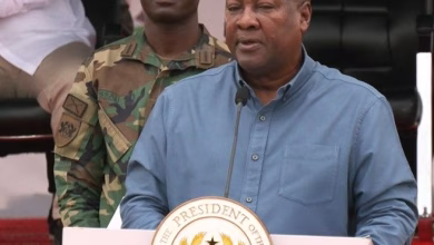 A man speaks at a podium bearing an official seal while a uniformed soldier stands behind him.