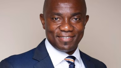 A close-up portrait shows a man in a dark suit, white shirt, and striped tie against a plain indoor background.