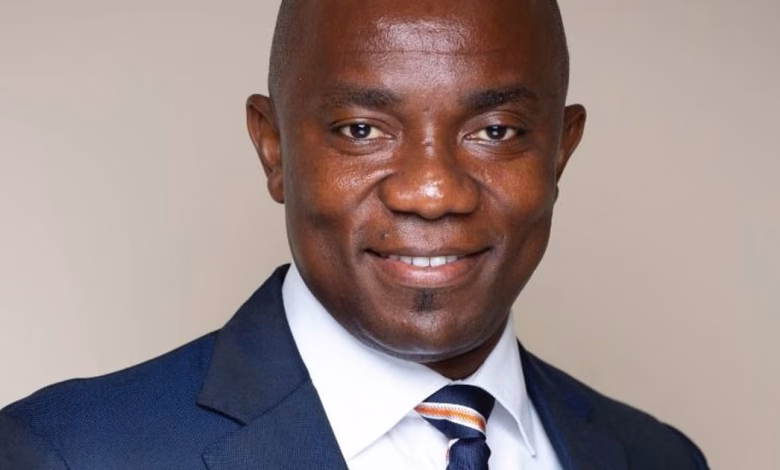 A close-up portrait shows a man in a dark suit, white shirt, and striped tie against a plain indoor background.