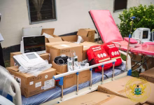 Medical equipment, hospital beds, boxed supplies, and emergency bags are arranged outside a building.