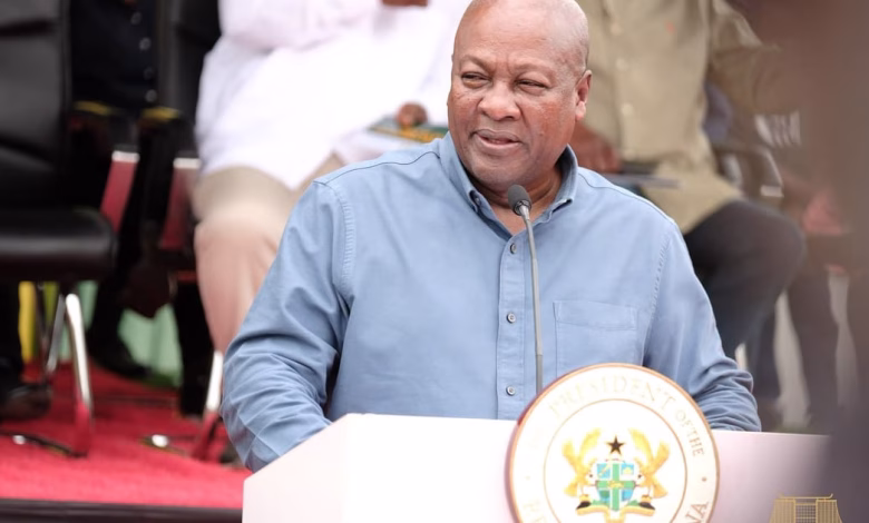 A man in a blue shirt speaks at a podium bearing a national seal, with seated people behind him.