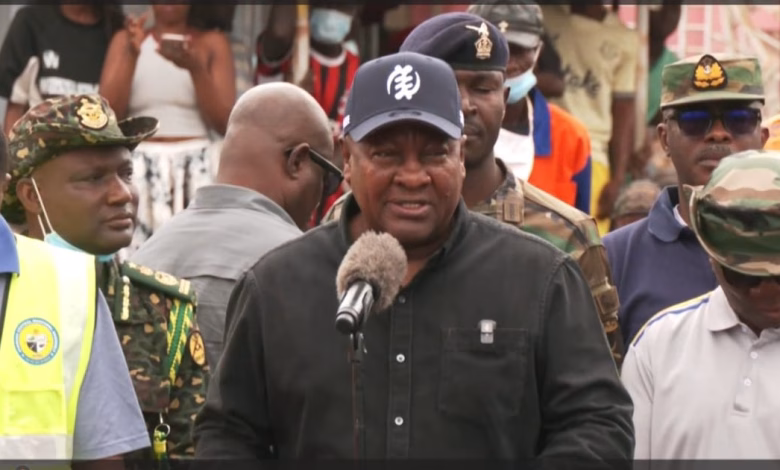 A man speaks into a microphone outdoors while surrounded by uniformed personnel and other attendees.