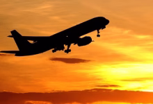 A silhouetted passenger airplane takes off against a vivid orange and yellow sunset sky.
