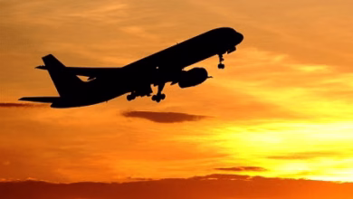 A silhouetted passenger airplane takes off against a vivid orange and yellow sunset sky.