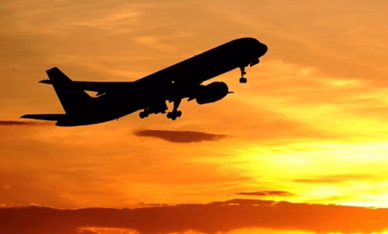 A silhouetted passenger airplane takes off against a vivid orange and yellow sunset sky.