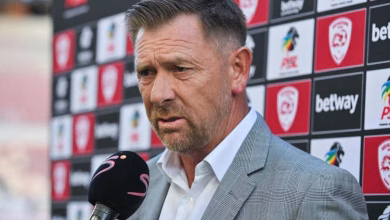 A man in a grey suit is being interviewed with a microphone in front of a sports sponsor backdrop.