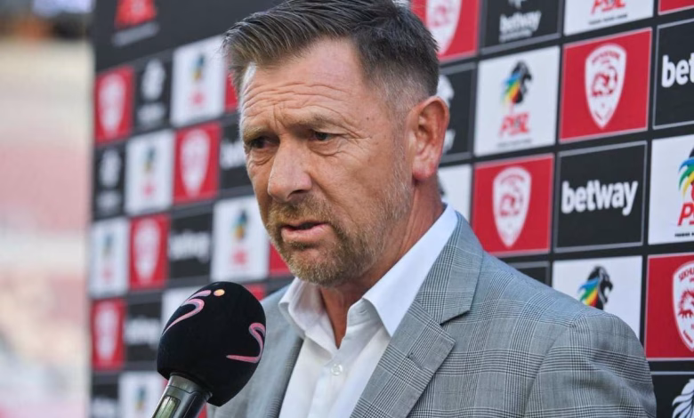 A man in a grey suit is being interviewed with a microphone in front of a sports sponsor backdrop.