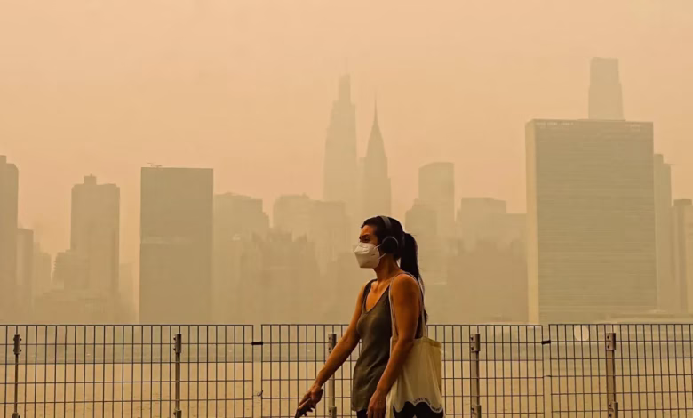 A person wearing a face mask walks beside a metal fence with a hazy city skyline in the background.