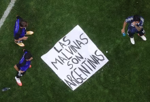 An overhead view shows three football players standing on a grass field around a large handwritten banner.