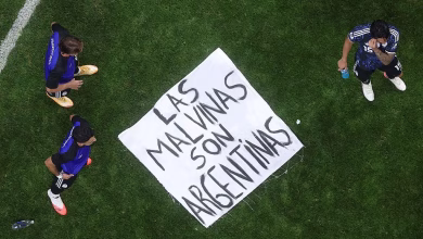 An overhead view shows three football players standing on a grass field around a large handwritten banner.