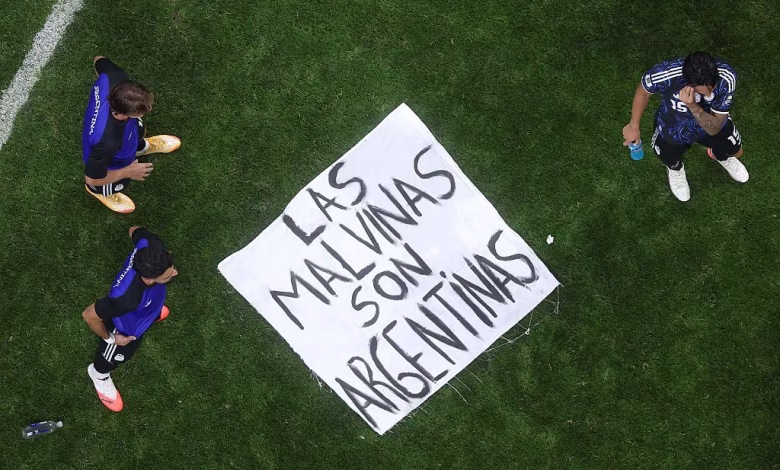 An overhead view shows three football players standing on a grass field around a large handwritten banner.