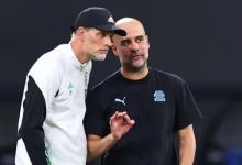 Two men in sportswear stand together on the sidelines, with one appearing to gesture while speaking.