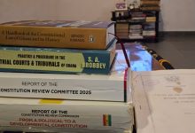 A stack of books and reports about Ghanaian constitutional law and review commissions is displayed on a table in an indoor setting.